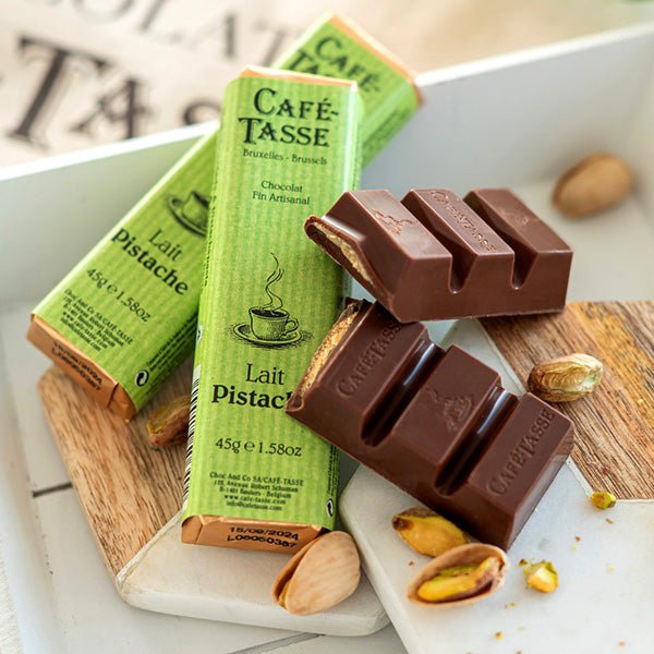Café Tasse Lait Pistache chocolate bars on a wooden board with packaging.