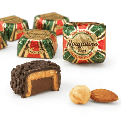 A close-up of chocolate confectionery products on a warm cream background, including several wrapped Nougatine candies, a cut open chocolate piece showing nut filling, and a hazelnut and almond. 