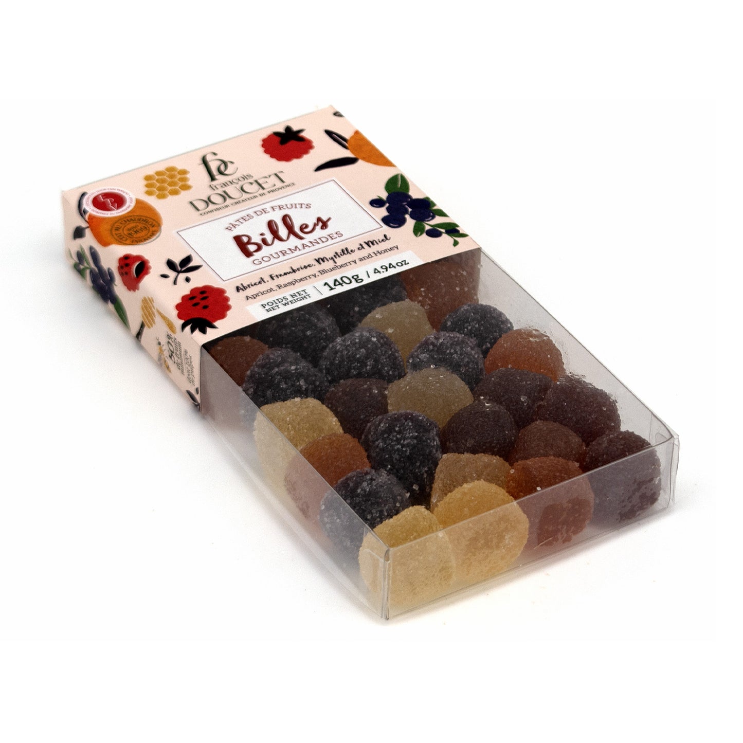 A clear plastic box of French fruit gummies with a decorative cream-colored paper label. The gummies inside are assorted shades of brown, beige, and dark purple.