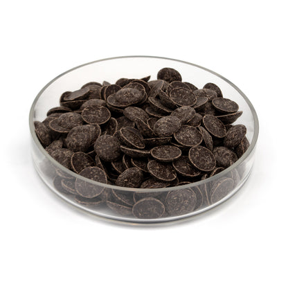 Glass bowl half filled with dark chocolate wafers on a white background