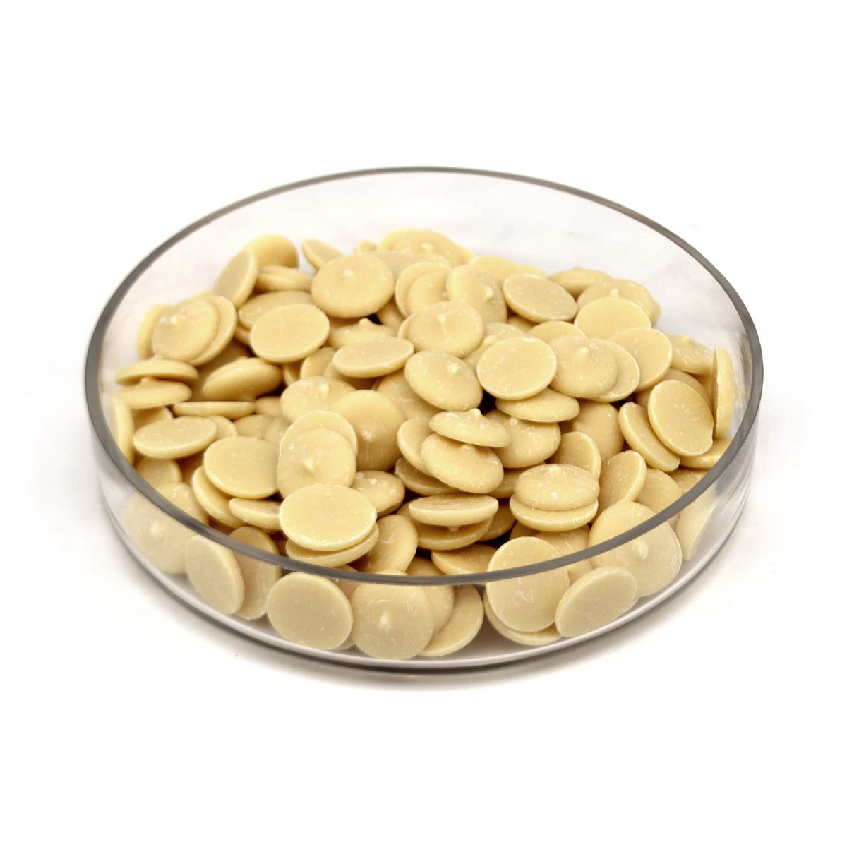 A clear round glass dish filled with small pale cream-colored disc-shaped white chocolate wafers, photographed on a clean white background.