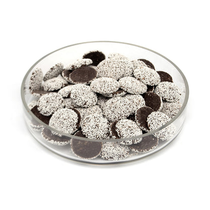 A clear round glass dish filled with dark brown chocolate discs topped with white sprinkles, photographed on a plain white background.