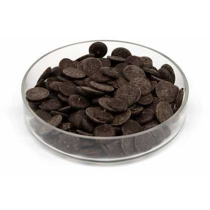Dark chocolate wafers piled in a clear glass bowl on a white background.
