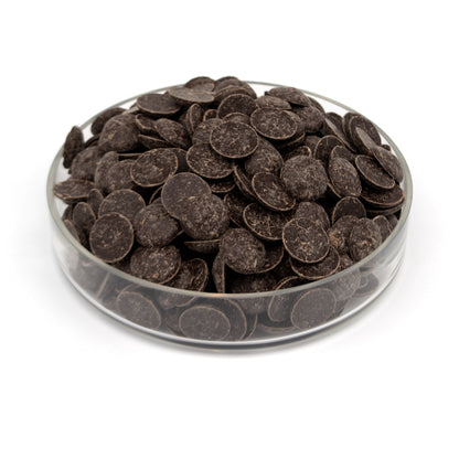Dark chocolate wafers piled in a clear glass dish on a white background.