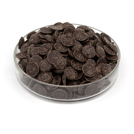 Dark chocolate wafers piled in a clear glass dish on a white background.
