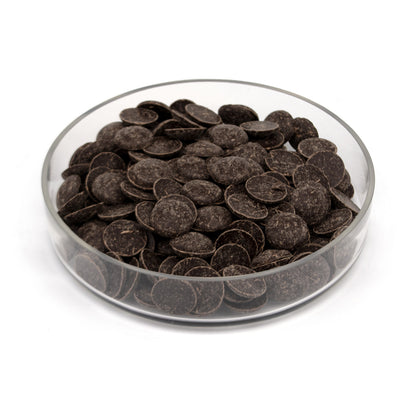 Dark chocolate wafers piled in a clear glass dish on a white background.