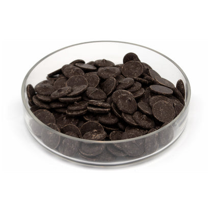 Dark chocolate wafers piled in a clear glass bowl on a white background.