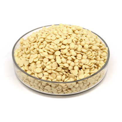 A clear round glass bowl filled with many small pale cream-colored chocolate discs, photographed on a clean white background.