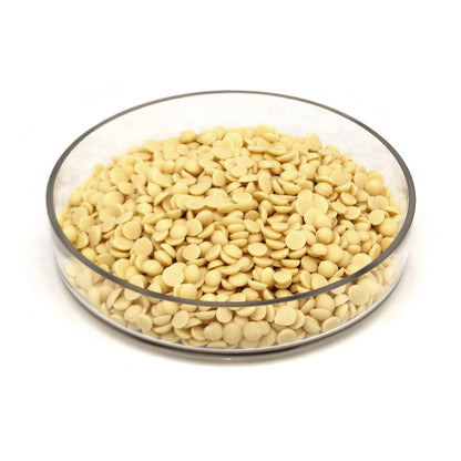 A clear glass bowl half filled with pale yellow disc-shaped chocolate chips, photographed on a clean white background.