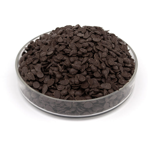 Dark chocolate discs piled in a clear glass bowl on a white background.