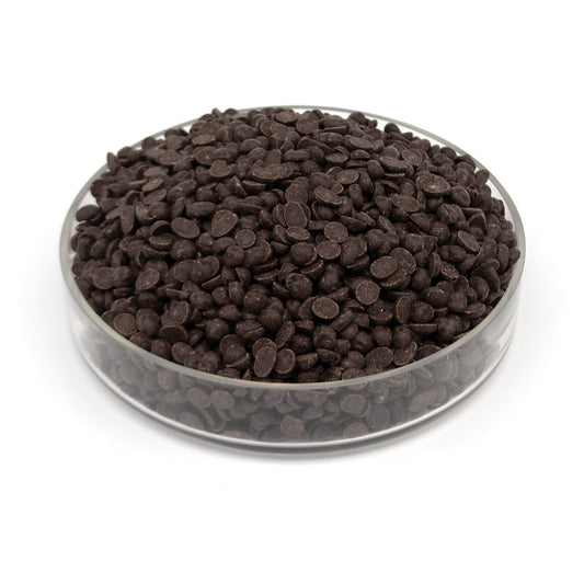 Dark chocolate discs piled in a clear round glass container on a white background.