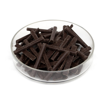 Dark chocolate batons piled in a clear glass bowl on a white background.