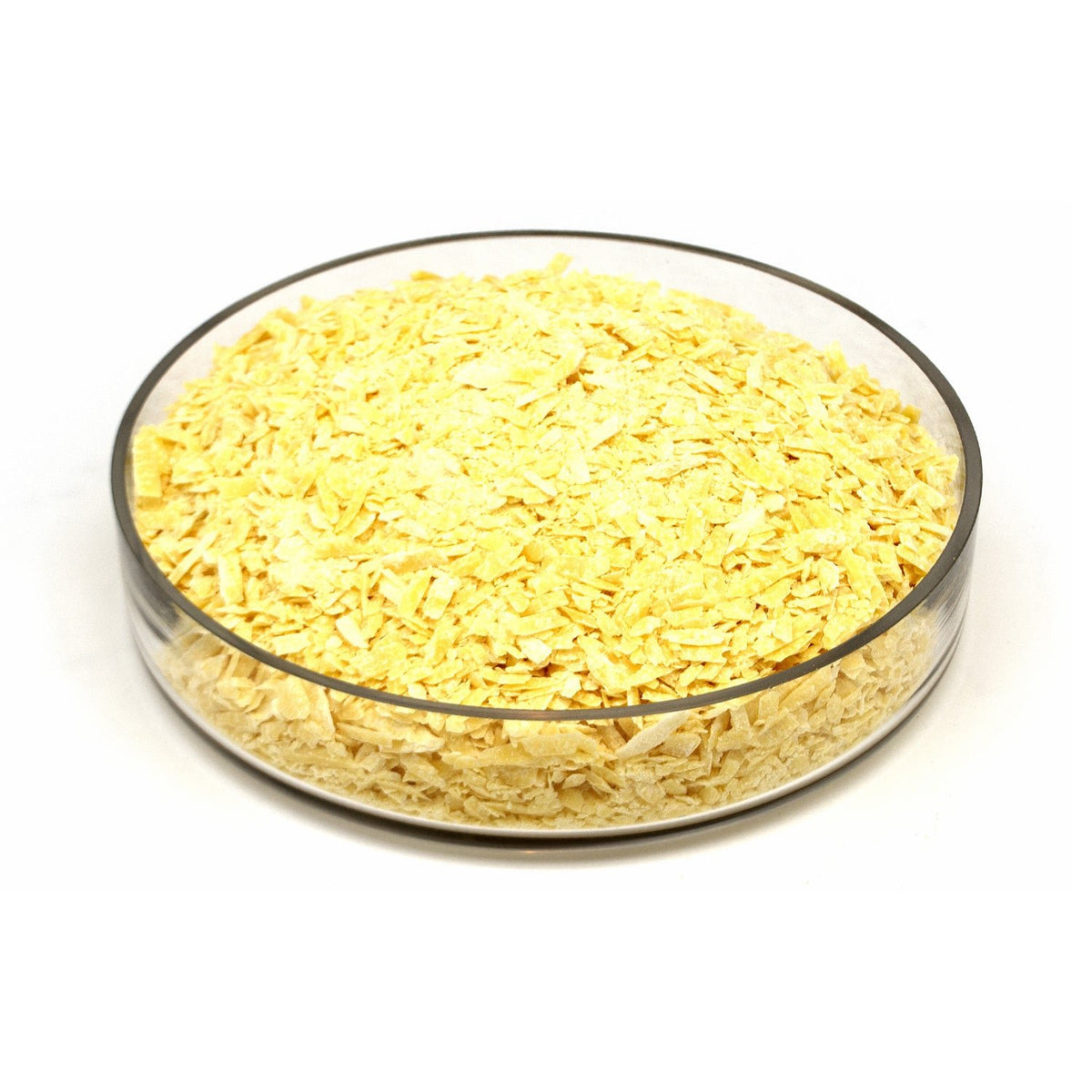 Cacao butter shavings piled in a clear round glass bowl on a white background.