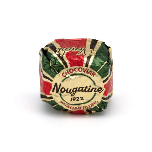 A single wrapped Nougatine hazelnut filling candy on a plain white background. The wrapper features a red, green, and cream sections, and the brand name 'Nougatine' is clearly visible in the center.